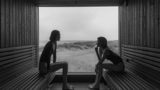 two woman facing each other sitting in a steam room with a black and white