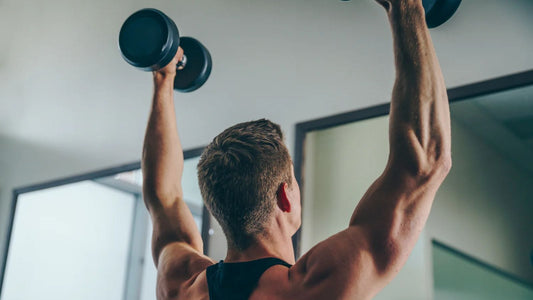 Man standing and shoulder pressing dumbbells during a workout.