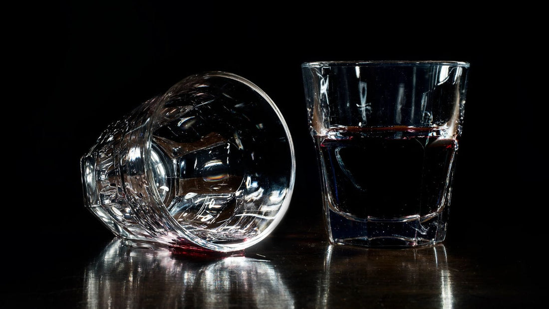 Two small drink glasses sitting on a wooden table against a black background