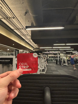 Hand holding a red packet labeled 'Oral Strip' in a gym setting